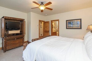 A bedroom with a bed, a wooden dresser, a television, a ceiling fan, a framed picture on the wall, and a door leading to another room. - Lakota Majesty | Pet Friendly | Hot Tub | Sauna | Across From Resort (Winter Park)