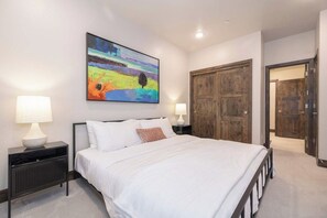 Ein Schlafzimmer mit einem großen Bett, zwei Nachttischen mit Lampen, einem farbenfrohen abstrakten Gemälde und einem Holzschrank.