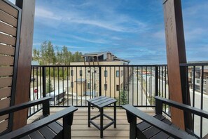 Een balkon met een tafel en twee stoelen, met uitzicht op een straat met gebouwen en bomen.