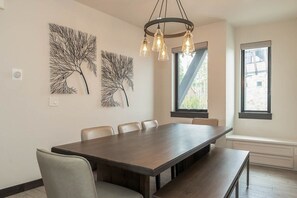 A dining area with a long table, chairs, and a bench. There are wall art pieces and a window with a view. - Arrow Reserve | Pet Friendly | Downtown Dream | Hot Tub (Winter Park)