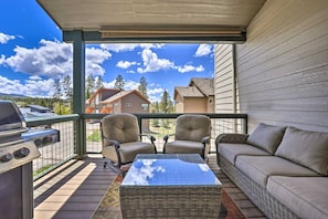 A covered outdoor area with a grill, two chairs, a sofa, and a view of houses in the background. - Rendezvous Retreat | Pet Friendly with Peak Vistas | Walk to Trails (Fraser)