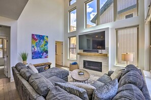 A spacious living room with a large gray sectional sofa, a flat-screen TV mounted above a fireplace, and a colorful abstract painting on the wall. - Rendezvous Retreat | Pet Friendly with Peak Vistas | Walk to Trails (Fraser)
