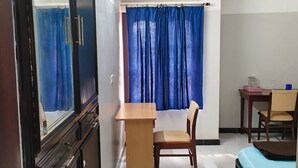 Quarto com cama, escrivaninha, cadeira, guarda-roupa e janela com cortinas.