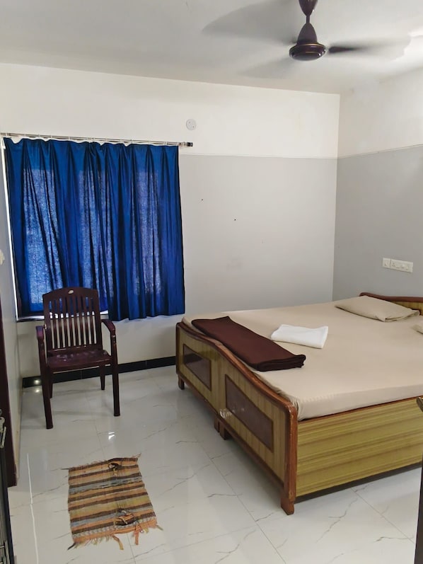 A bedroom with a bed, a chair, a window with curtains, and a ceiling fan.