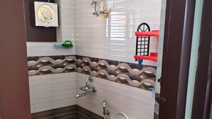 Casa de banho com sanita, secador de mãos, chuveiro e parede revestida a mosaicos.