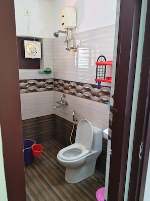 Ein Badezimmer mit Toilette, einem Händetrockner, einer Duschbrause und einer gefliesten Wand.