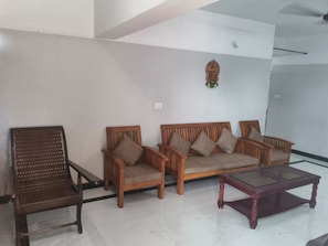 A living room with a sofa set, a wooden armchair, and a glass coffee table.