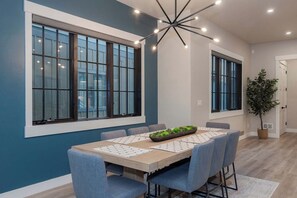 A modern dining room with a large table, blue chairs, and a ceiling light fixture. - Gather & Glow | Downtowan House | Private Hot Tub (Winter Park)
