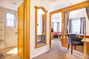 Habitación de hotel con puerta de madera, un espejo, un área de comedor con mesa y sillas, y un sofá.