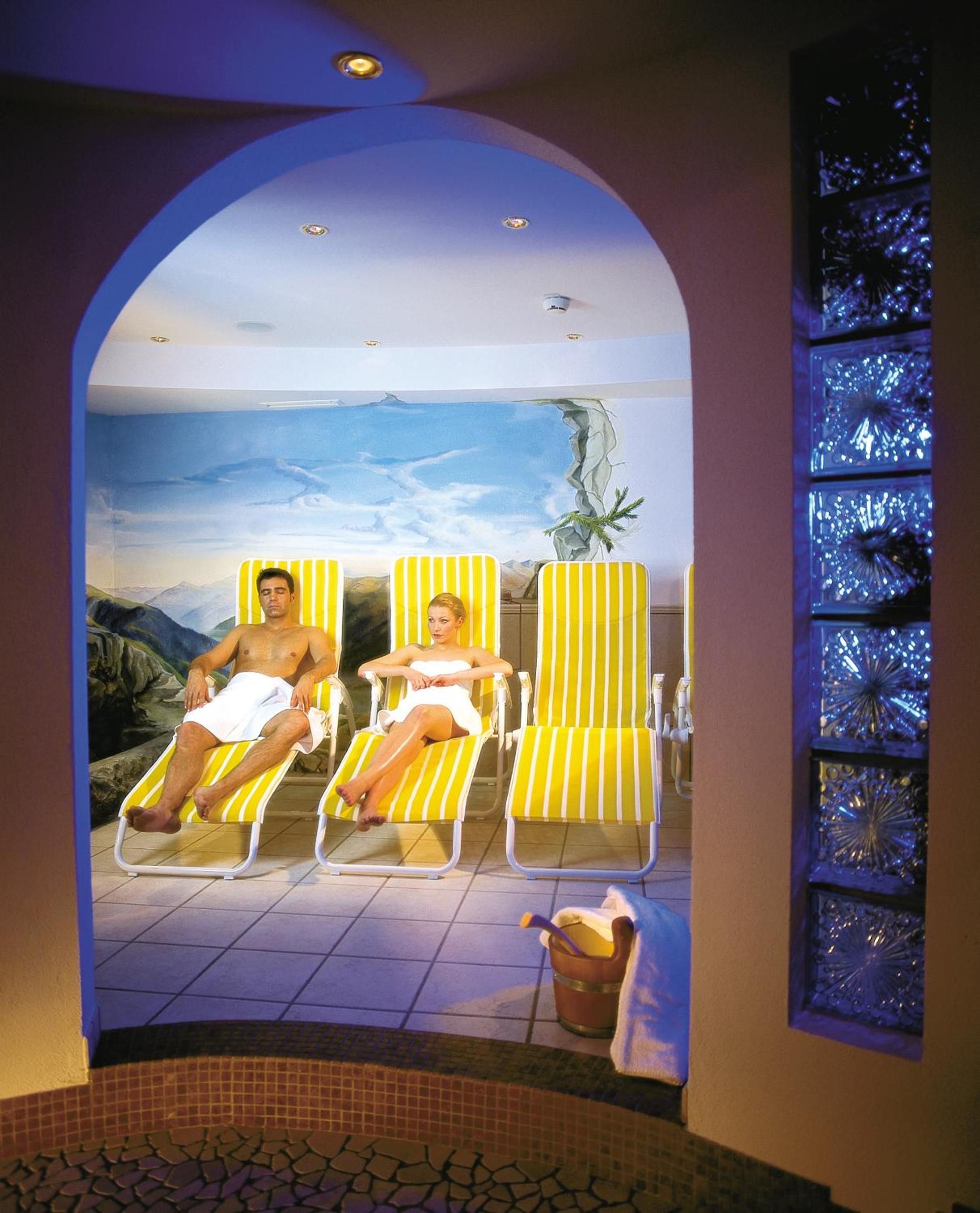 A spa area with a view of mountains, two sun loungers, and a decorative wall with a plant.