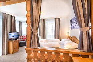 Habitación de hotel con una cama de madera, cortinas, un televisor y vistas al exterior.