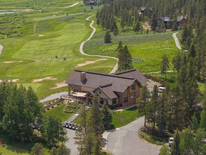 Eine Lodge mit einem großen Gebäude, umgeben von einem Golfplatz und dichtem Wald.