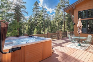 Ein Whirlpool auf einer Holzterrasse mit Tisch und Stühlen, umgeben von einem Wald.