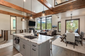 A spacious kitchen with a large island, a dining area with a table and chairs, and a living room with a sofa and a fireplace. - Lakota Evergreen | Slope Views | Private Hot Tub (Winter Park)