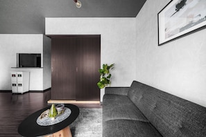 A modern living room with a dark wooden door, a grey sofa, a coffee table with a decorative centerpiece, and a plant. - Edgewater Terrace 211 (Sapporo)