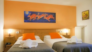 A hotel room with two beds, orange pillows, a painting of rabbits, and a radiator. - Indren Hus - Residence (Alagna Valsesia)