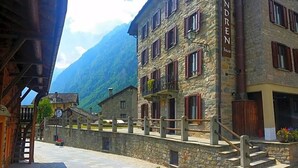 A stone building with multiple windows and balconies, a wooden staircase, and a stone wall with a metal railing. - Indren Hus - Residence (Alagna Valsesia)