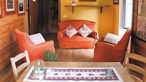 A cozy room with a wooden interior, a dining table with a placemat, and orange upholstered chairs. - Indren Hus - Residence (Alagna Valsesia)