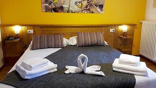 A hotel room with a bed, pillows, a painting, and towels arranged on the bed. - Indren Hus - Residence (Alagna Valsesia)