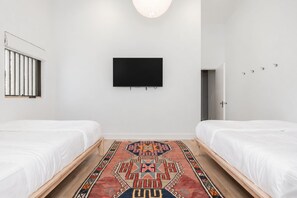 Et moderne hotelværelse med to senge, et fladskærms-TV, et mønstret tæppe og et vindue med persienner.