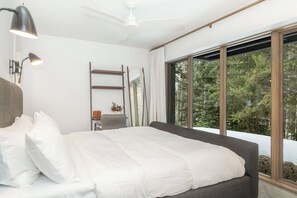 A bedroom with a large bed, a ceiling fan, a desk with a chair, and a window with a view of trees. - Creekside Retreat | Private Hot Tub | Secluded Modern Retreat (Winter Park)