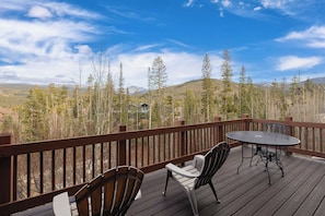 A deck with a table and chairs, overlooking a forested landscape with mountains in the distance. - Bear Den | Private Deck | Rocky Mountain Views (Winter Park)