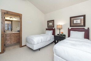 Une chambre d’hôtel avec deux lits simples, une commode en bois, un miroir et des œuvres d’art encadrées accrochées aux murs.