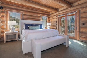 A log cabin bedroom with a large bed, two bedside tables, and a view of the outdoors through a sliding glass door. - Lakota Cedarcrest | Large & Luxe | Private Hot Tub | Resort Views (Winter Park)
