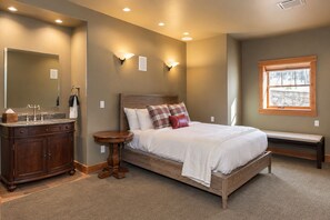 Een slaapkamer met een houten bed, nachtkastje, dressoir, een bankje en een raam.
