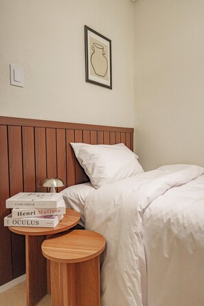 A neatly made bed with white linens, a wooden headboard, and a small bedside table with a lamp and books.