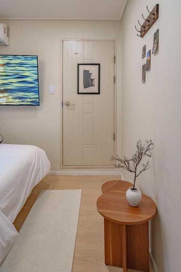 A bedroom with a bed, a bedside table with a vase, a door, and a wall with framed pictures.