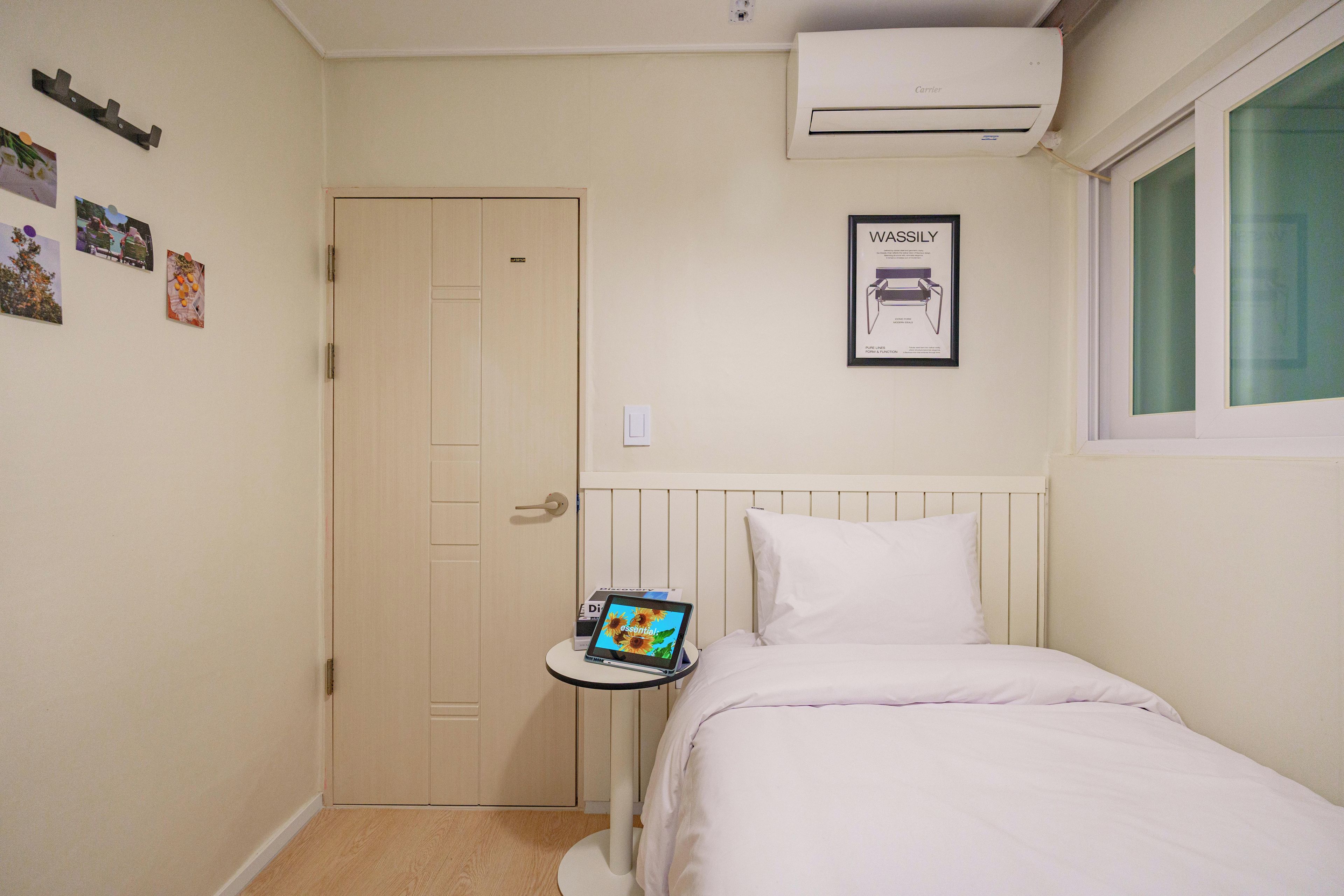 Een slaapkamer met een bed, een nachtkastje met een tablet, een deur en een airconditioning.