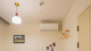 A room with a bed, a desk with a chair, an air conditioner, and a door. - WAYHOME (Seoul)