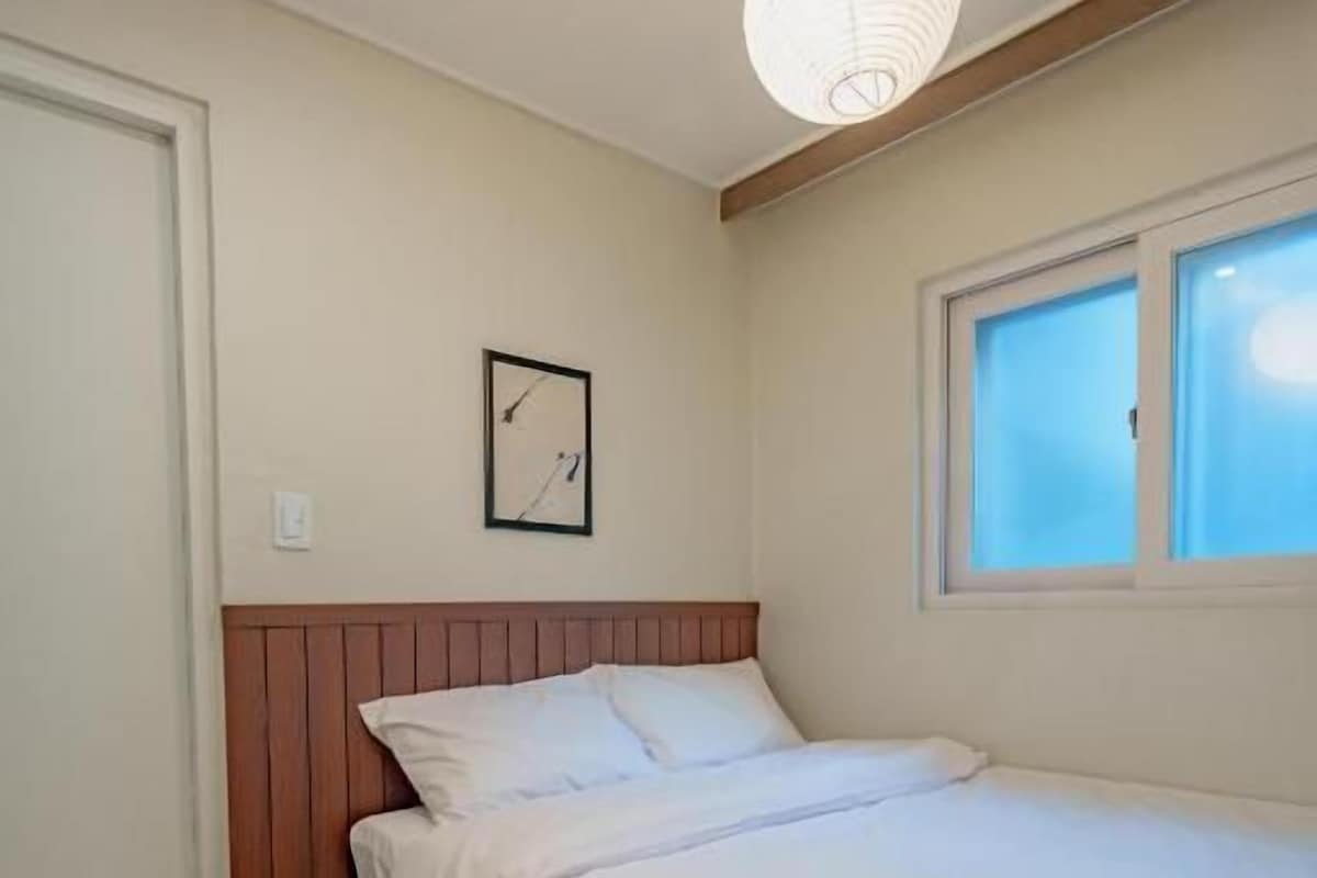 Un dormitorio con cama, ventana, un reloj de pared y una lámpara colgante.
