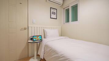 Un dormitorio con cama, una mesita de noche con una computadora portátil, una ventana y un equipo de aire acondicionado.