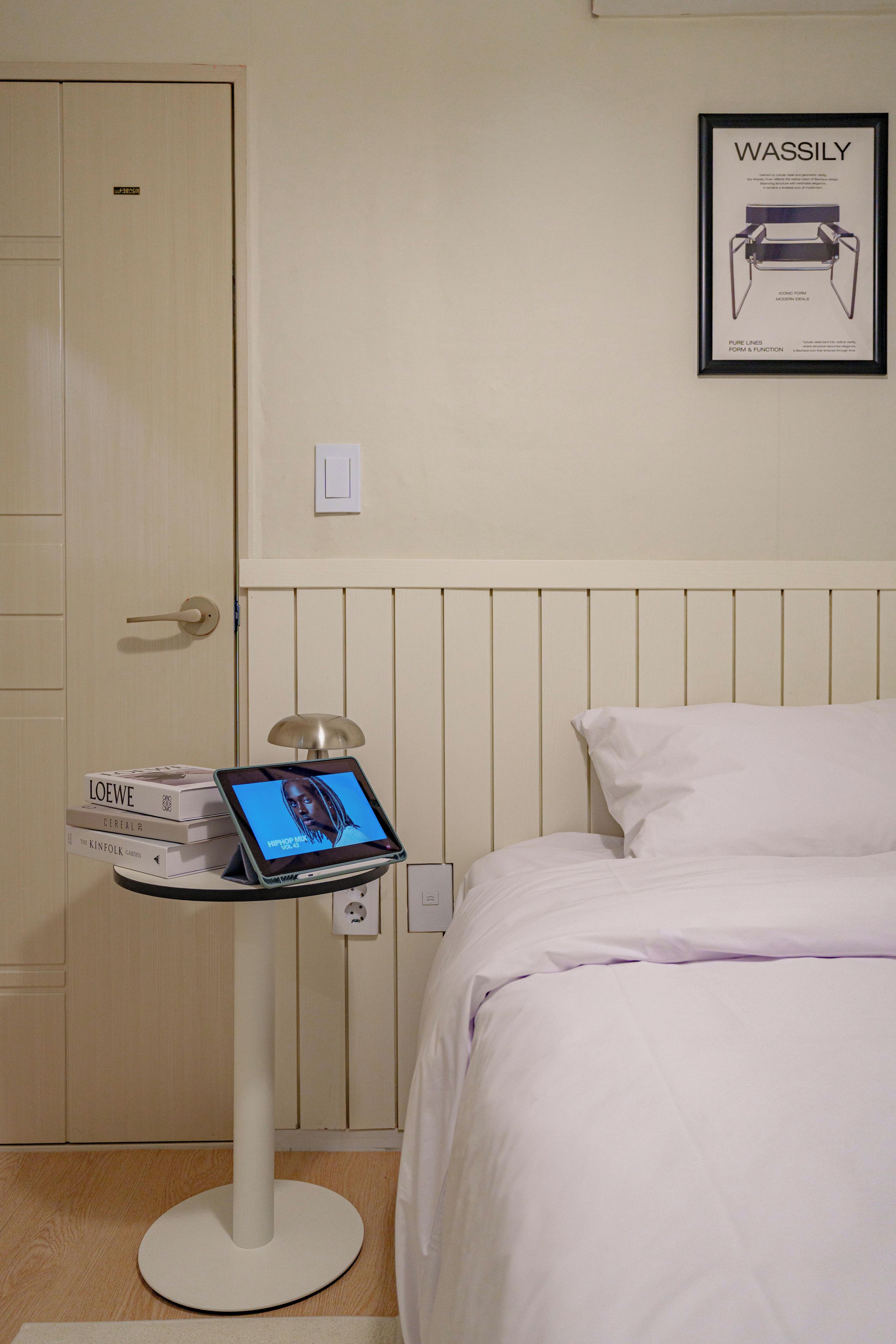Habitación de hotel con una cama, una mesita de noche con lámpara y un cuadro colgado en la pared.
