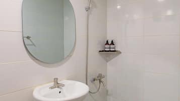 A bathroom with a white sink, a round mirror, a shower, and a shelf with toiletries.