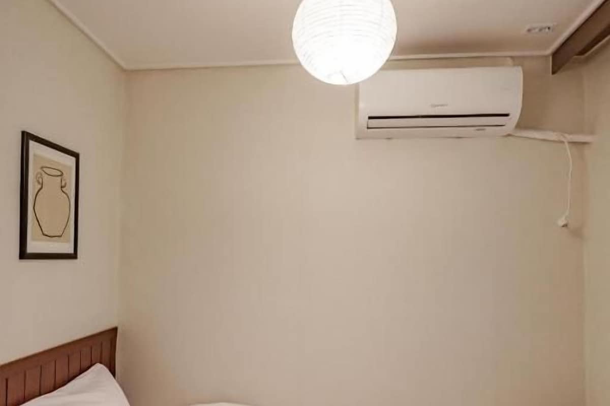 Una camera d'albergo con un letto, un comodino, una lampada a sospensione e un condizionatore d'aria.