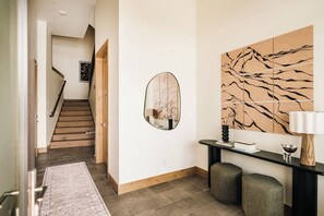 A modern hallway with a staircase, a round mirror, and a console table with a lamp. - Lakota Lookout | Private Hot Tub | Slope Views (Winter Park)