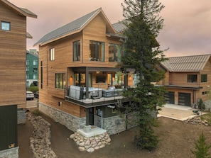 A two-story wooden house with a balcony, a stone foundation, and a garage. - Dilly Dally Chalet | Private Hot Tub | Colorful & Modern Downtown Home (Winter Park)