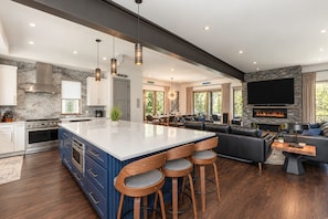 A modern kitchen with a large island, bar stools, and a dining area with a fireplace. - Dilly Dally Chalet | Private Hot Tub | Colorful & Modern Downtown Home (Winter Park)