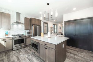 A modern kitchen with stainless steel appliances, a central island, and a dark door. - Solstice Abode | Pet Friendly | Private Hot Tub | Prime Location (Winter Park)