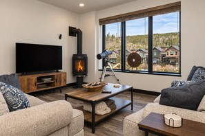 A living room with a fireplace, a television, and a large window with a view of houses. - Solstice Abode | Pet Friendly | Private Hot Tub | Prime Location (Winter Park)