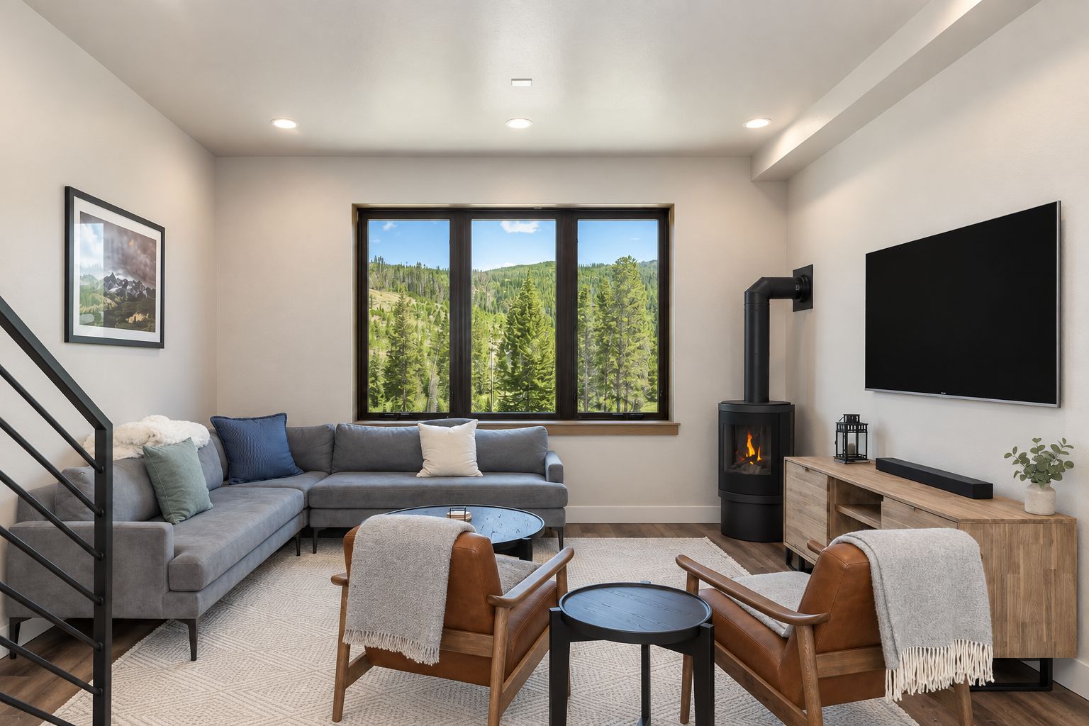 A modern living room with a sofa, a fireplace, a TV, and a large window with a forest view.