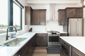 A modern kitchen with stainless steel appliances, dark wooden cabinets, and a large window providing natural light. - Sunset Roost | Hot Tub | Roof Top Deck (Winter Park)