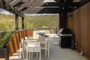 An outdoor patio with a table and chairs, a grill, and a view of a forested area. - Sunset Roost | Hot Tub | Roof Top Deck (Winter Park)