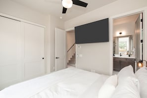 A bedroom with a bed, a flat-screen TV mounted on the wall, a staircase leading to a bathroom, and a ceiling fan. - Sunset Roost | Hot Tub | Roof Top Deck (Winter Park)
