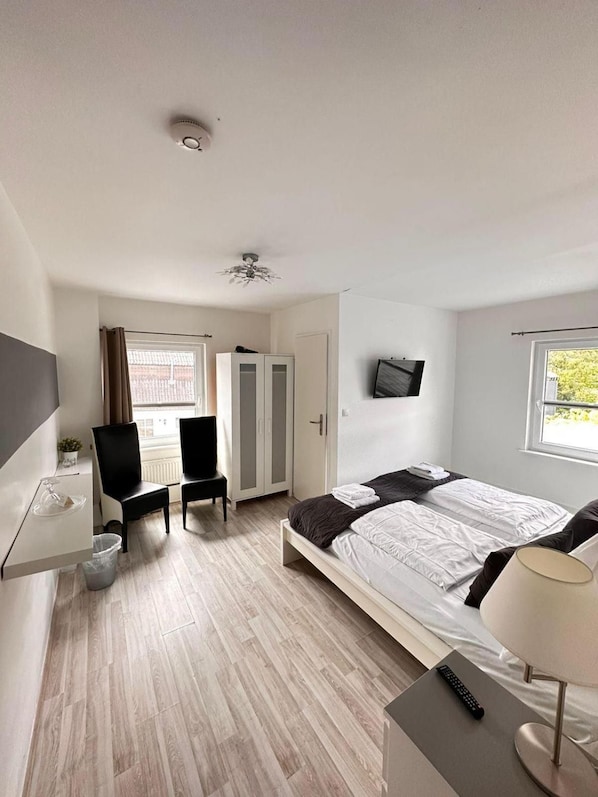 Un dormitorio con cama, escritorio, silla, televisor y ventana.