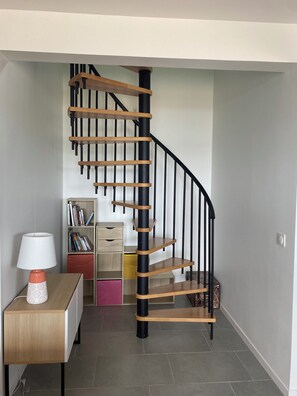 Ein modernes Interieur mit einer Wendeltreppe, einem Holztisch mit Lampe und einem Bücherregal.