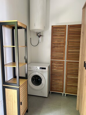 Ein kleiner Hauswirtschaftsraum mit einer Waschmaschine, Holzregalen und einem Warmwasserbereiter.